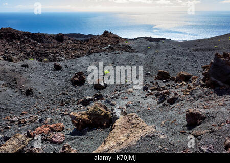 Los Volcanes de Teneguía, Fuencaliente, La Palma. Una vista del paesaggio arido con lava le formazioni rocciose che guarda al mare blu profondo. Molto poca vegetazione, è in grado di crescere in condizioni difficili di questo ambiente. Si tratta di una giornata soleggiata con qualche veloce movimento di nuvole in contrasto con il blu del cielo. Foto Stock