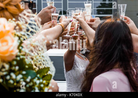 Gli ospiti dei matrimoni tintinnanti bicchieri da champagne con gli sposi novelli in background. Foto Stock