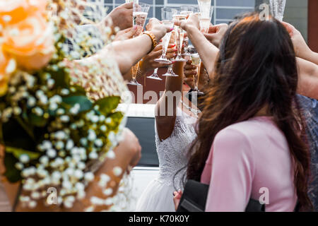 Gli ospiti dei matrimoni tintinnanti bicchieri da champagne con gli sposi novelli in background. Foto Stock