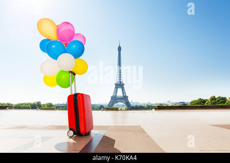 Foto di palloncini multicolori mazzo legato al rosso valigia, in piedi su una strada contro la torre eiffel Foto Stock