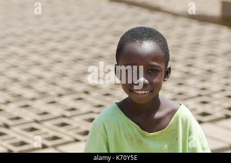 Piccolo bambino africano sorridente all'esterno dietro di mattoni - il lavoro minorile nozione Foto Stock