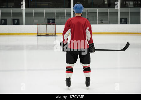 Vista posteriore a lunghezza piena di hockey su ghiaccio giocatore in piedi alla pista di pattinaggio Foto Stock