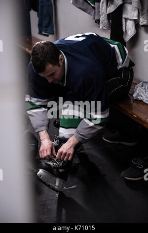 Voce maschile di hockey su ghiaccio di legatura giocatore skate seduti in spogliatoio Foto Stock