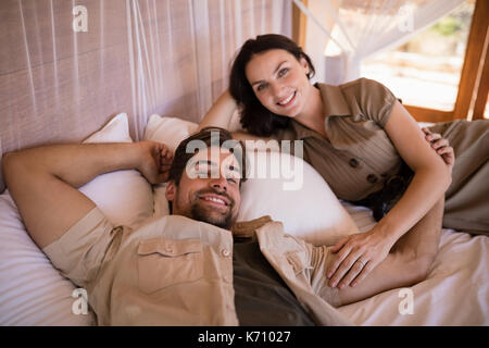 Ritratto di Coppia sorridente mentre giaceva sul letto a baldacchino durante la vacanza di safari Foto Stock
