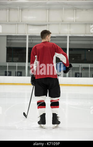 Vista posteriore maschile di hockey su ghiaccio giocatore con casco e bastone a rink Foto Stock