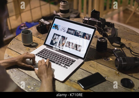 Tagliate le mani dell uomo con la fotocamera utilizzando il portatile in tavola nella caffetteria Foto Stock