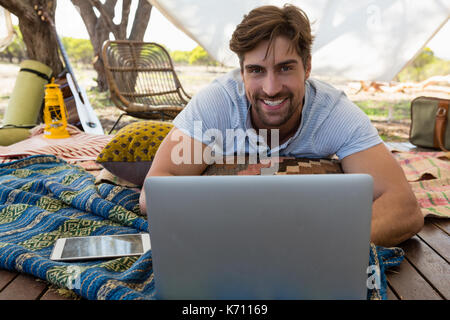 Ritratto di giovane sorridente uomo utilizzando laptop in tenda Foto Stock