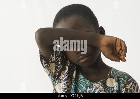 Little Boy africana chiede aiuto coprendo il viso con il suo braccio, isolato su bianco Foto Stock