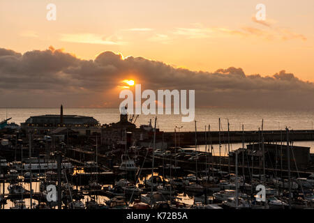 Inghilterra, Ramsgate. Alba sul Canale Inglese e Ramsgate Royal Harbour. Strato di nubi sull orizzonte con sun scoppio attraverso il piccolo spazio. Parte - silhouette di edifici in primo piano. Foto Stock