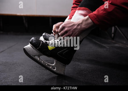 Bassa sezione maschio del giocatore di hockey su ghiaccio di legatura pattino in spogliatoio Foto Stock