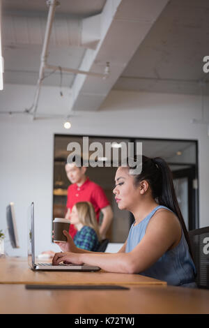 Vista laterale di imprenditrice con i suoi collaboratori utilizzando laptop a tavola in office Foto Stock