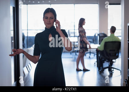 Giovane imprenditrice dai colleghi parlando al telefono in ufficio Foto Stock