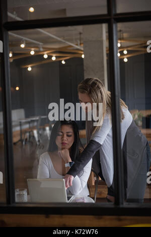 Imprenditrice con il collega discutendo su laptop visto attraverso il vetro di office Foto Stock