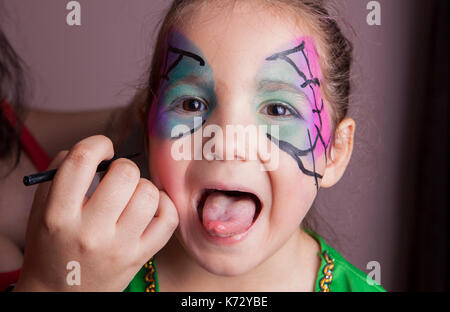 Bambina con la lingua di fuori mentre essa è composta da make-up artist Foto Stock