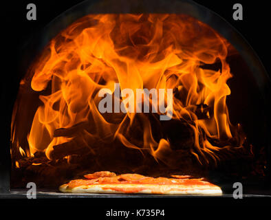 La cottura della pizza come lames salto da una sfolgorante log in una racchiusi in contenitori metallici di forno a legna Foto Stock