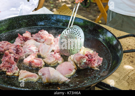 Mano d'uomo con la schiumarola ribaltamento di carne di pollo frittura in subbuglio l' olio d' oliva in piatto largo. Cucina spagnola spagnolo paella o jambalaya. all'aperto, famil Foto Stock