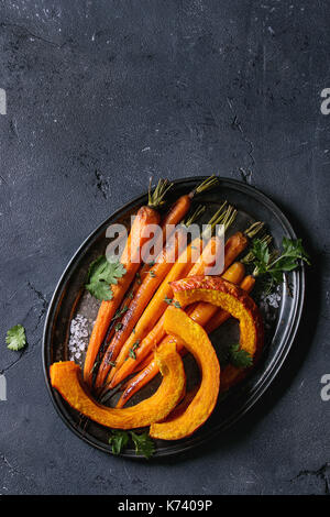 Giovane arrosto tutta la carota e fette di zucca con verdi e sale marino. servita su vintage vassoio di metallo nero su sfondo texture. vista superiore con spac Foto Stock