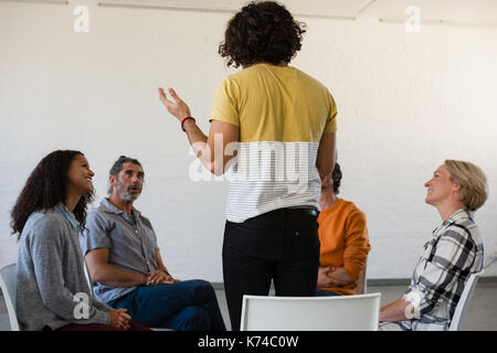L'uomo gesticolando mentre discute con gli amici seduti su una sedia in classe d'arte Foto Stock