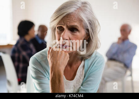 Tensionata senior femmina con amici in background in classe d'arte Foto Stock