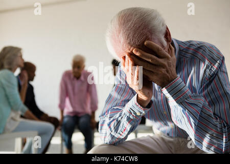 Senior Uomo con testa in mano seduti sui capelli con gli amici discutendo in background in classe d'arte Foto Stock