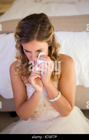 Angolo di alta vista della sposa triste piangere mentre è seduto dal letto di casa Foto Stock