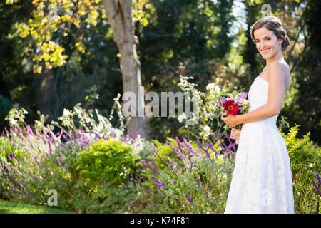 Ritratto di sorridere sposa bouquet di contenimento mentre si sta in piedi sul campo in cantiere Foto Stock