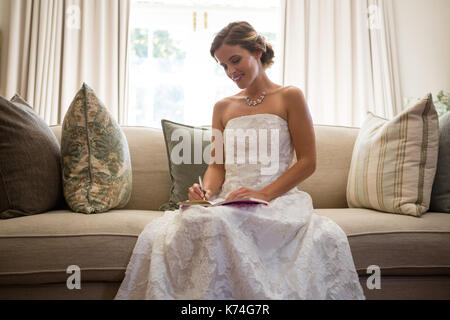 Basso angolo vista della sposa bella scrittura in diario comodamente seduti sul divano di casa Foto Stock