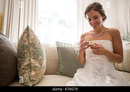 Basso angolo vista della bella sposa guardando l'anello nuziale comodamente seduti sul divano di casa Foto Stock