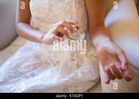 Sezione mediana della sposa profumo di spruzzatura sulla mano mentre seduti a casa Foto Stock