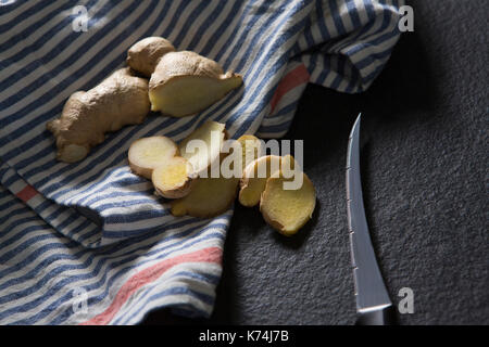 Close-up di zenzero affettato con coltello e tovagliolo su sfondo nero Foto Stock
