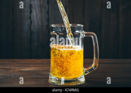 La birra artigianale versata in una pinta di vetro sullo sfondo di legno. bellissimo sfondo dell'OKTOBERFEST Foto Stock