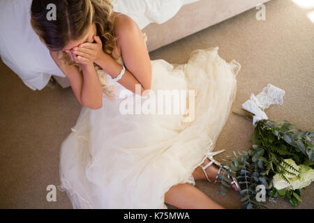 Angolo di alta vista della sposa in abito da sposa a piangere mentre è seduto dal letto di casa Foto Stock