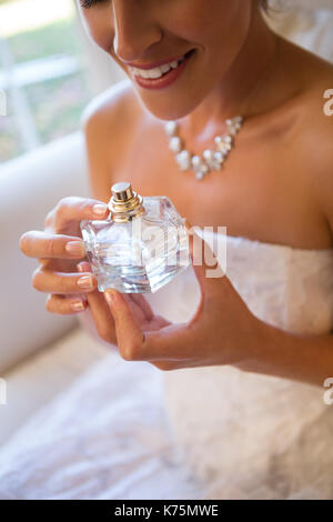 Sezione mediana della sposa sorridente holding spruzzatore di profumo mentre è seduto sulla poltrona di casa Foto Stock