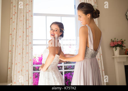 Sorridente damigella regolazione sposa abito da sposa in sala di montaggio Foto Stock