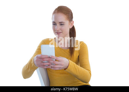 Sorridente imprenditrice tenendo selfie mentre è seduto su una sedia contro uno sfondo bianco Foto Stock