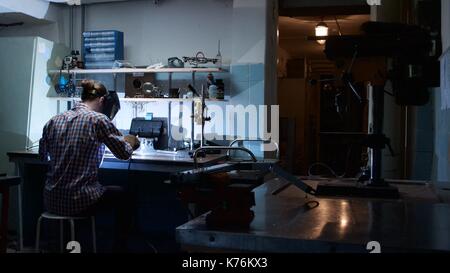 Vista posteriore del saldatore professionale uomo con torcia e la maschera protettiva in acciaio di saldatura con scintilla in officina. saldatore vista posteriore. vista posteriore ritratto uomo che indossa la maschera protettiva di saldatura in officina Foto Stock