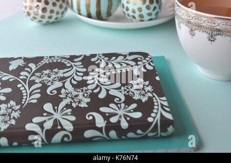 Decorate le uova di pasqua con motivi floreali notebook e la tazza di tè alla menta su aqua teal blu sfondo turchese con spazio di copia Foto Stock