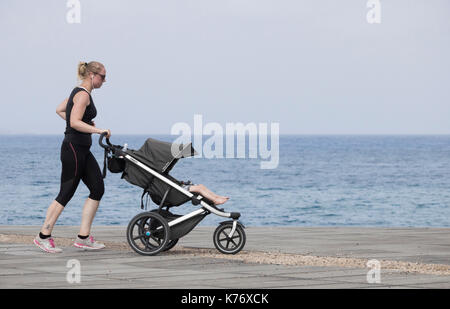 Donna jogging con il neonato/bambino nel passeggino/passeggino in Spagna Foto Stock