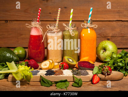 Assortimento di frutta e verdura frullati in bottiglie di vetro con cannucce su sfondo di legno. Foto Stock
