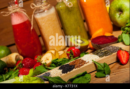 Assortimento di frutta e verdura frullati in bottiglie di vetro con cannucce su sfondo di legno. Foto Stock