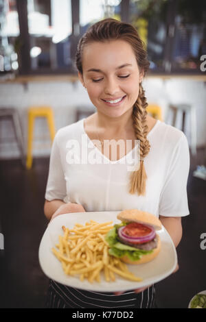 Sorridente giovane cameriera tenendo fresco il cibo spazzatura piastra al cafe Foto Stock