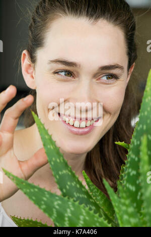 Giovane donna toucing aloe vera pianta e ridere Foto Stock