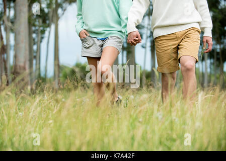 Giovane tenendo le mani e camminare attraverso l'erba alta, sezione bassa Foto Stock