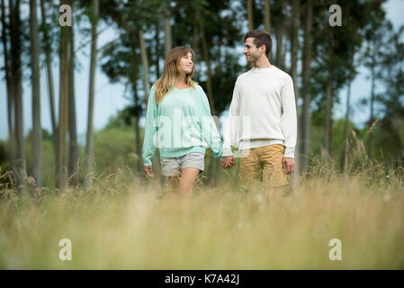 Coppia giovane camminando mano nella mano attraverso erba alta Foto Stock