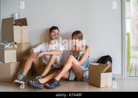 Coppia giovane seduto in casa di nuova costruzione circondata da scatole di cartone Foto Stock