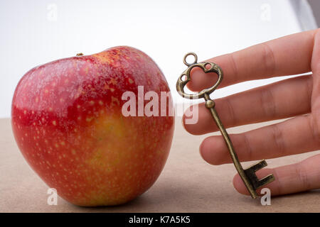 Mano che tiene una chiave accanto a una mela rossa Foto Stock