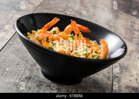 Tagliatelle e gamberetti con verdure in nero ciotola sul tavolo di legno Foto Stock