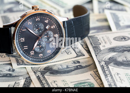 Primo piano della bella orologio moderno giacente su sfondo costituito da un centinaio di dollari di notes Foto Stock