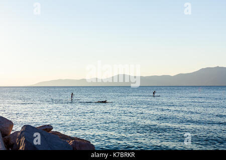 Silhouette di due surfisti sulla scheda di pala sono attraversando il mare calmo. Foto Stock