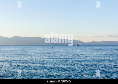 Silhouette di due surfisti sulla scheda di pala sono attraversando il mare calmo. Foto Stock